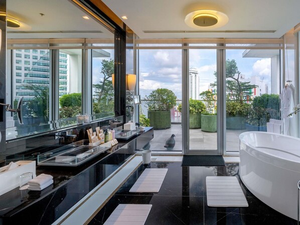 A modern bathroom with a large bathtub, a vanity with a mirror, and a view of the city through large windows. - Novotel Manila Araneta City Hotel (Quezon City)