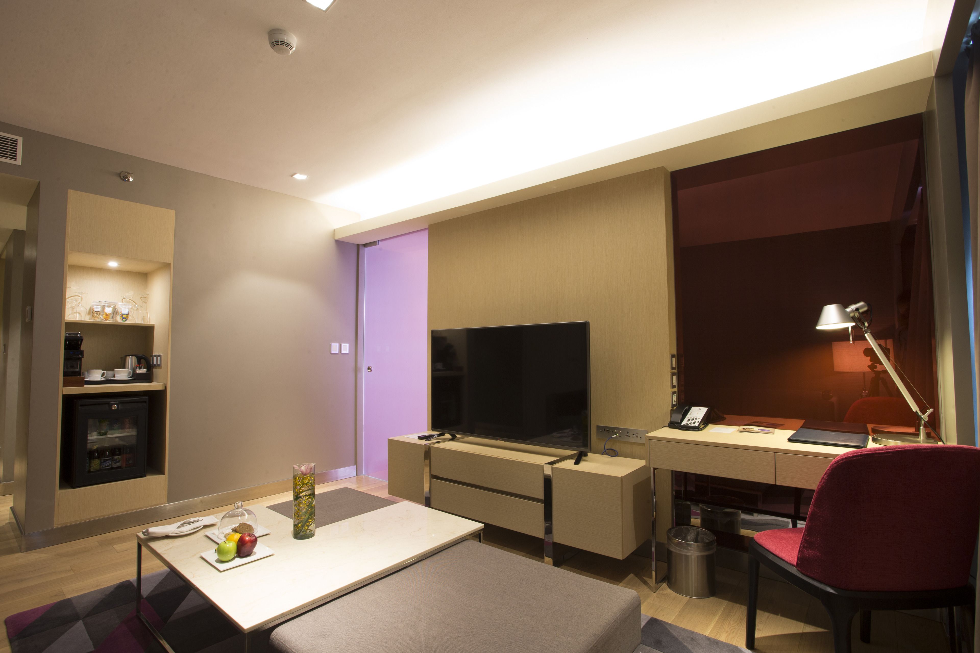 Ein Hotelzimmer mit Flachbildfernseher, Schreibtisch mit Computer, Stuhl, einer kleinen Küchenzeile und einem Mülleimer.