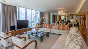 A modern living room with a large flat-screen TV, a sofa set, a coffee table, and a dining area with a chandelier. - Novotel Manila Araneta City Hotel (Quezon City)