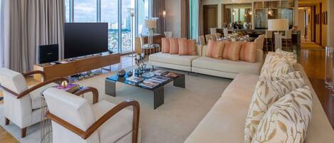 A modern living room with a large flat-screen TV, a sofa set, a coffee table, and a dining area with a chandelier.