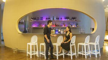 Una zona de bar con sillas blancas y estantes llenos de botellas.