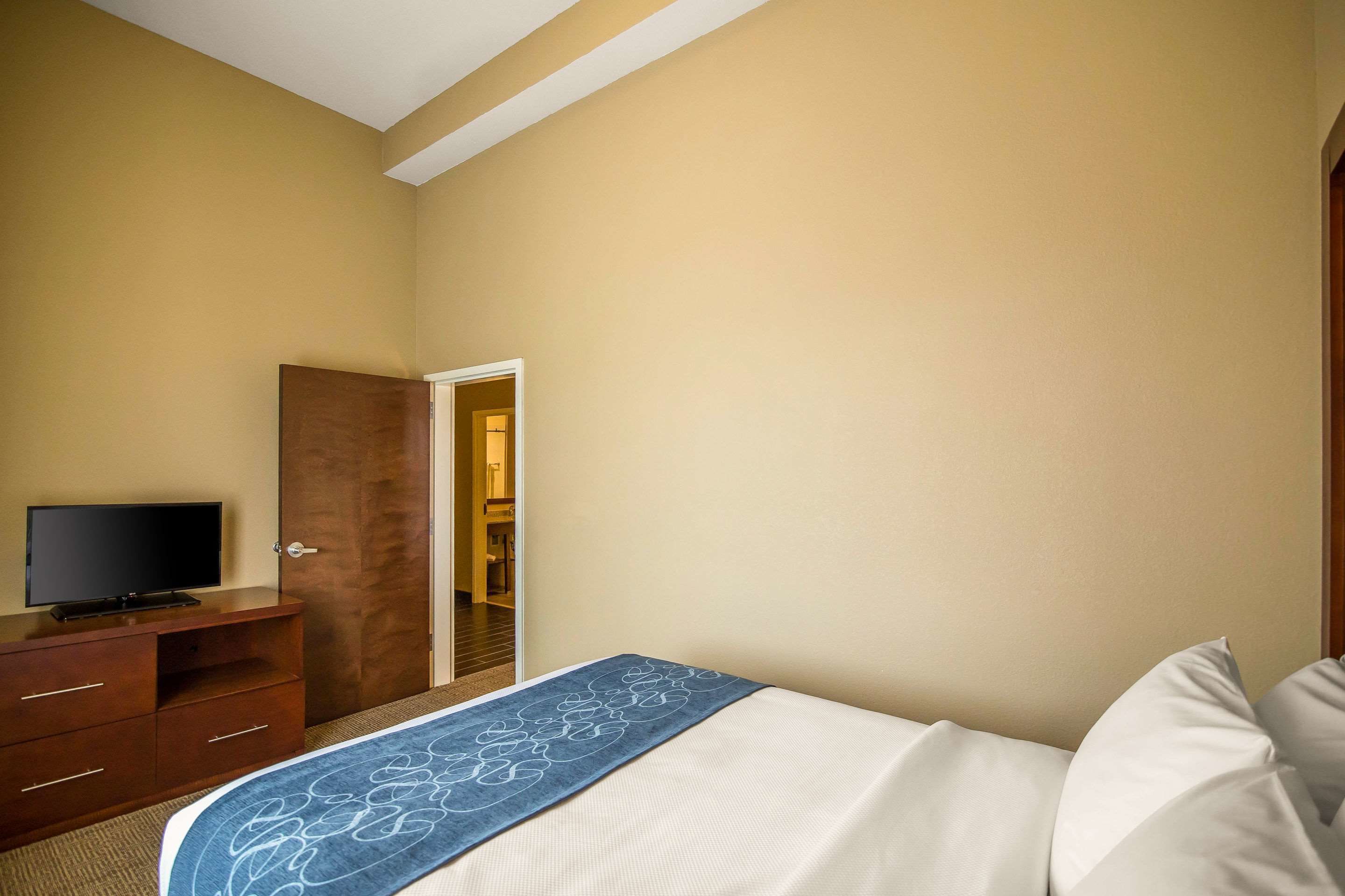 A hotel room with a bed, a TV on a wooden dresser, and a door leading to another room.
