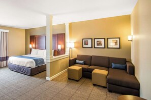 A hotel room with a bed, a sofa, a coffee table, and a wall with framed pictures. - Comfort Suites Dodge City (Dodge City)
