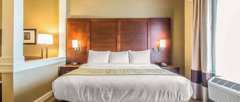 A hotel room with a large bed, two bedside lamps, a nightstand, and a window with curtains.