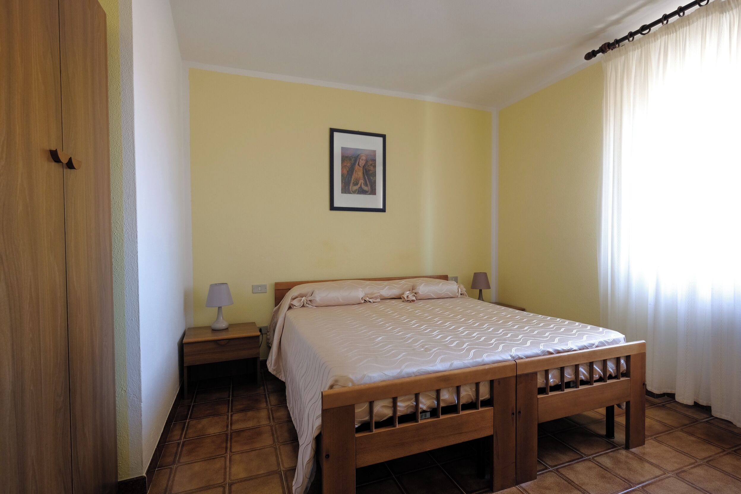 A bedroom with a wooden bed, a nightstand, a lamp, and a framed picture on the wall.