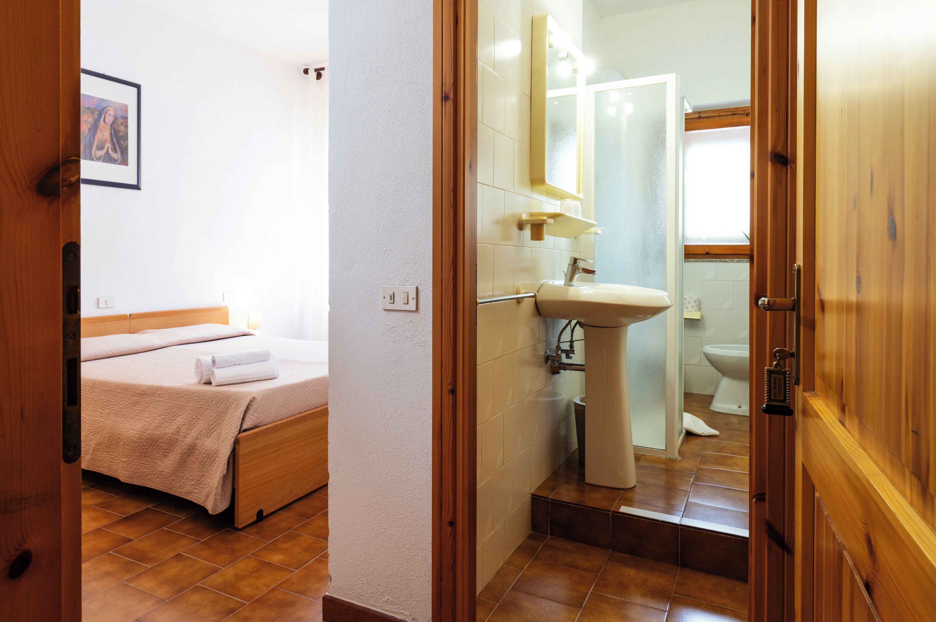 Ein Schlafzimmer mit Bett, ein Badezimmer mit Waschbecken und Toilette sowie eine Holztür.