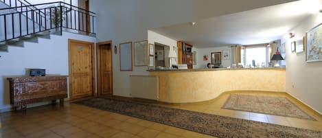 A spacious living area with a staircase, a reception desk, and a large rug.