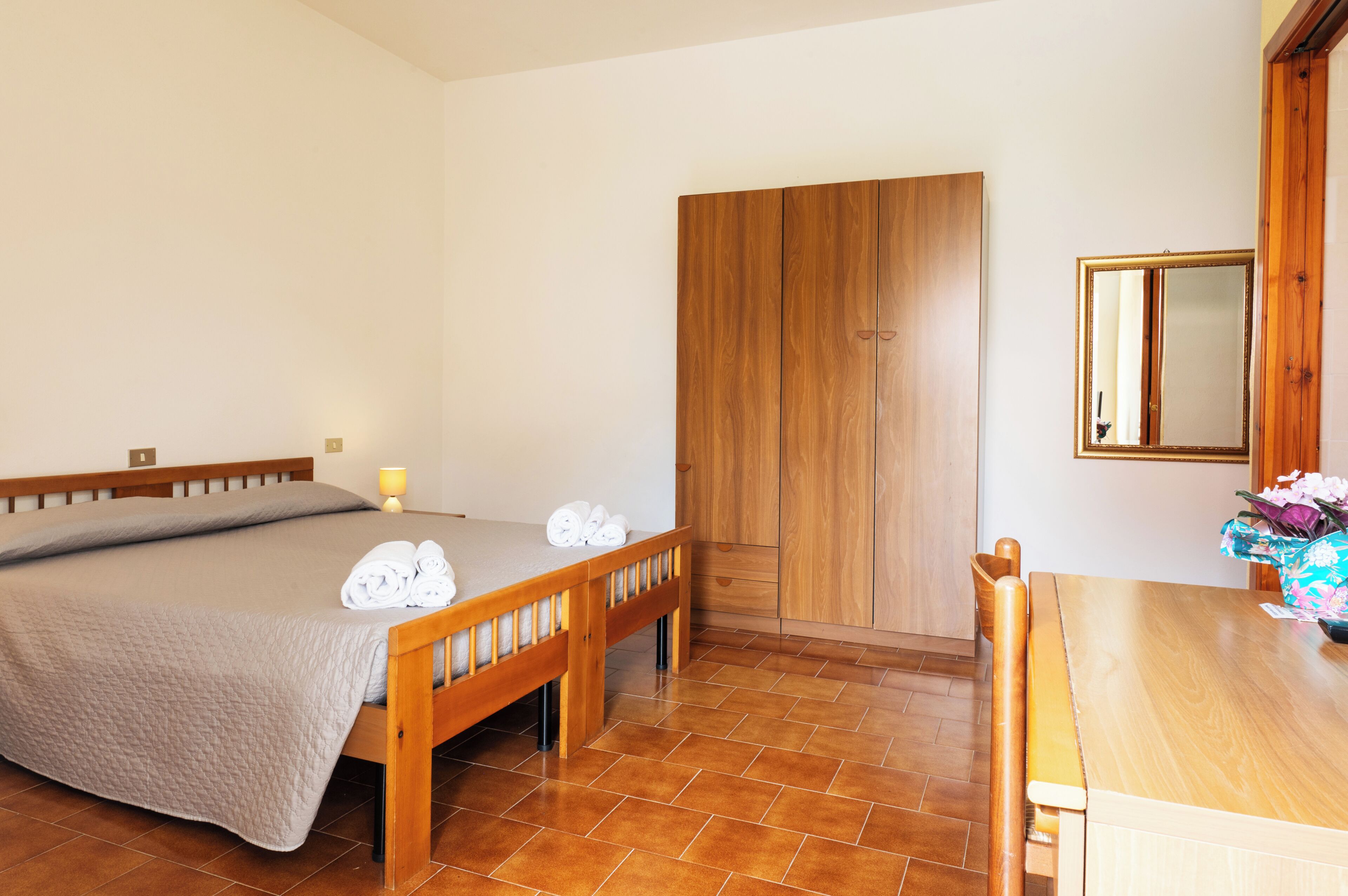 A bedroom with a bed, a wooden wardrobe, a table, and a chair.