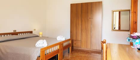 A bedroom with a bed, a wooden wardrobe, a table, and a chair.