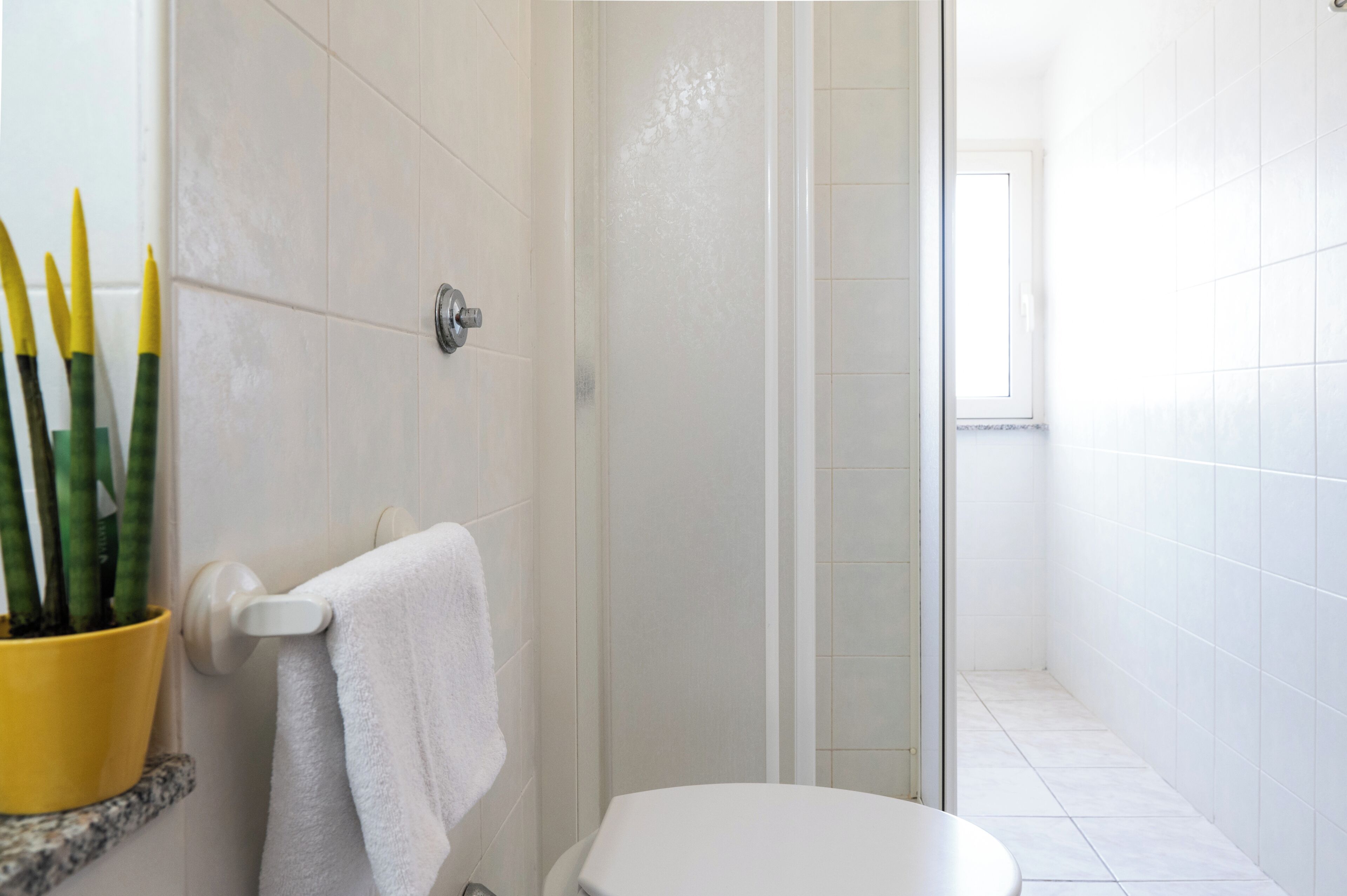 Een badkamer met een wit toilet, een douchegedeelte en een gele plant op een plank.