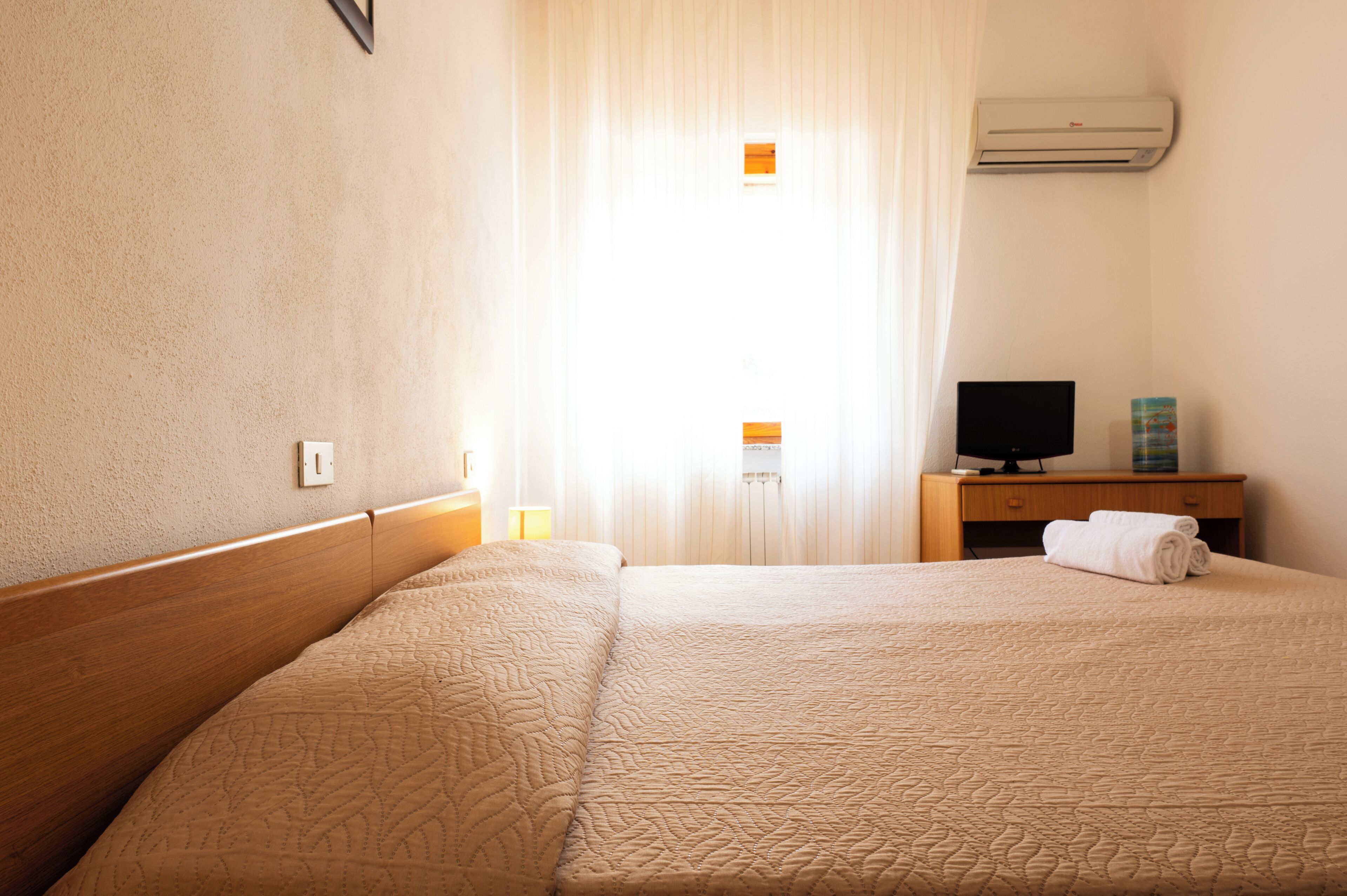 Una habitación de hotel con una cama grande, un televisor sobre una mesita de noche de madera y una ventana con cortinas.
