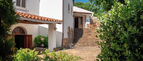 A building with a white facade, a tiled roof, and a stone staircase leading to a door.