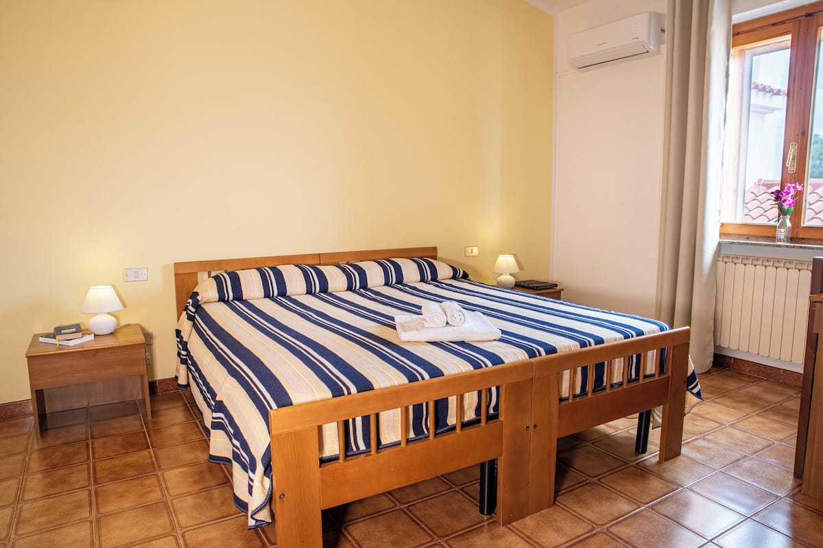 Una camera da letto con un letto in legno, biancheria a righe, due comodini con lampade, una finestra con tende e un termosifone.