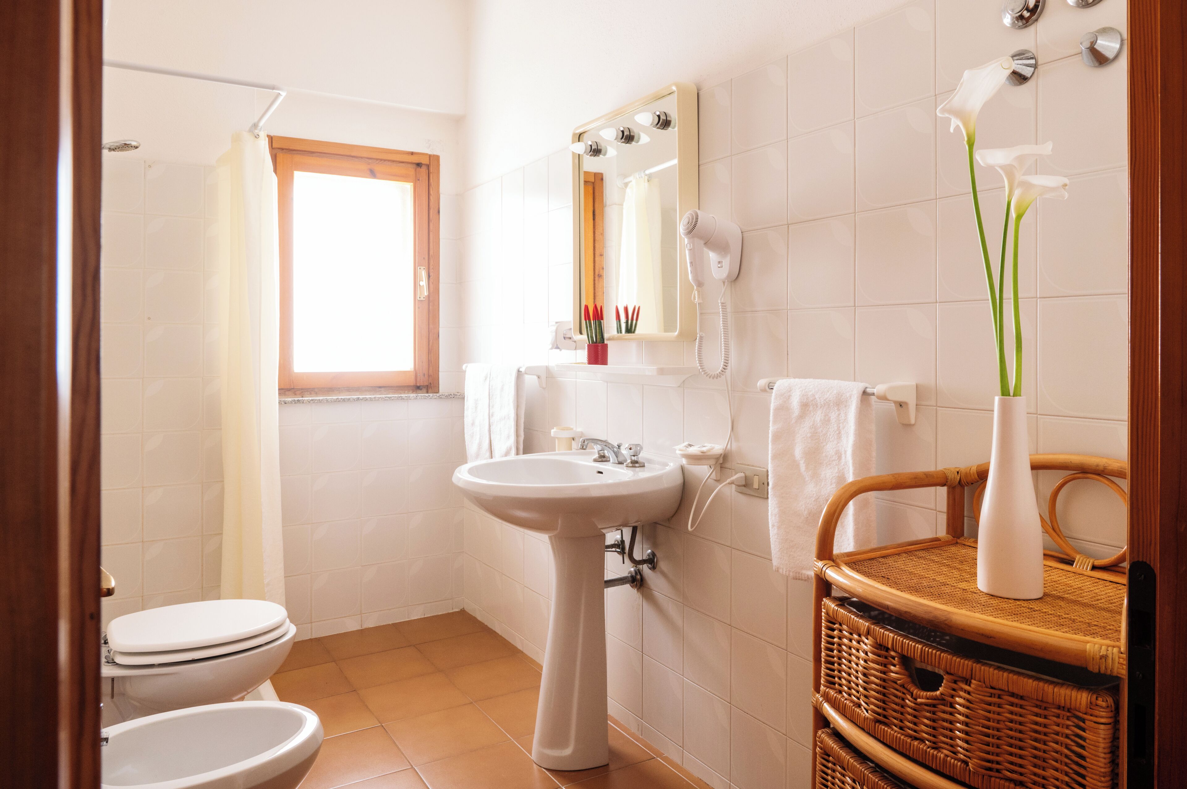 A bathroom with a sink, two toilets, a shower, a mirror, and a wicker basket.