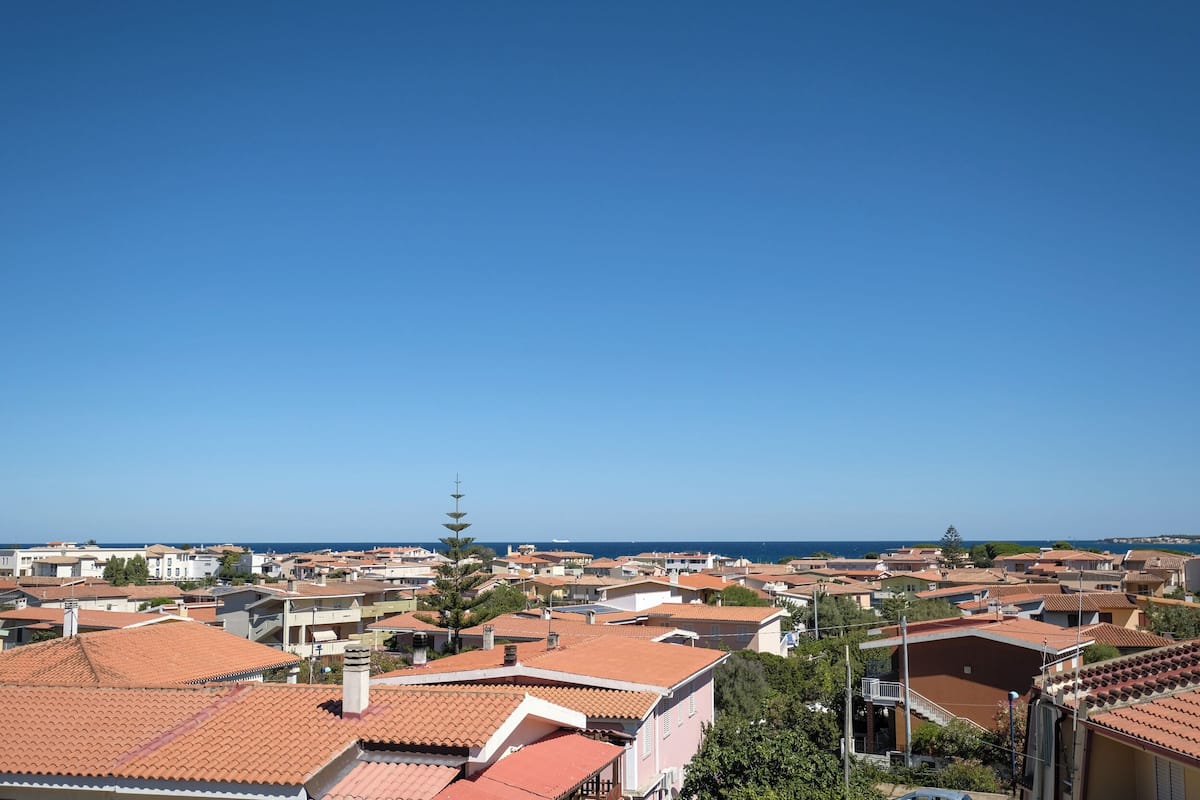 Una zona residenziale costiera con case dai tetti in terracotta, cielo sereno e vista aperta sul mare.