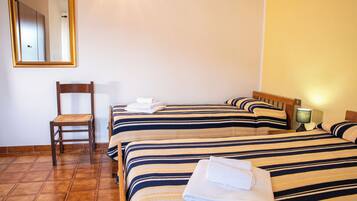 Habitación de hotel con dos camas, una silla, un espejo y una mesita de noche con lámpara.