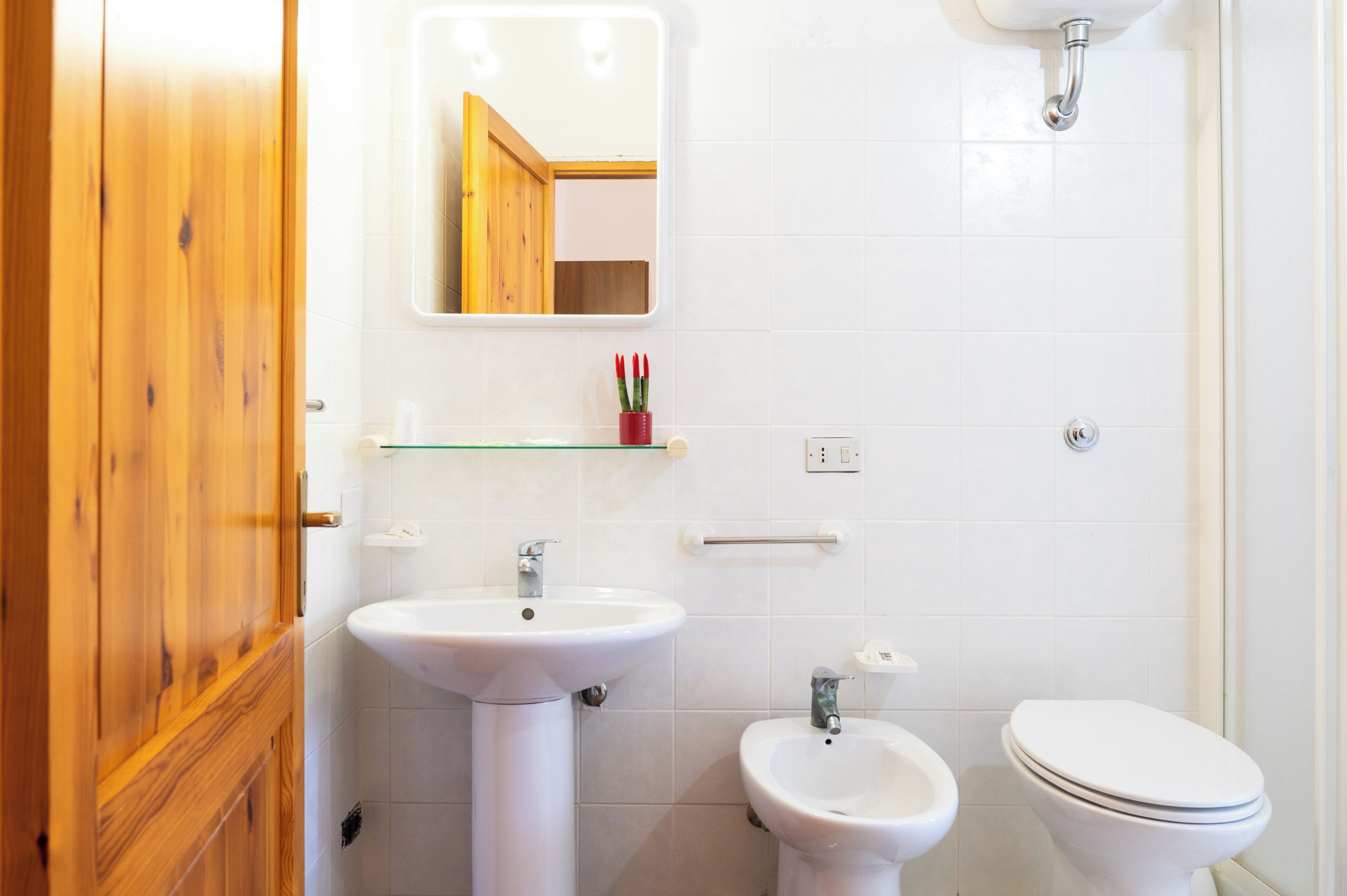 Een badkamer met een houten deur, een witte wastafel, een bidet, een toilet en een spiegel.