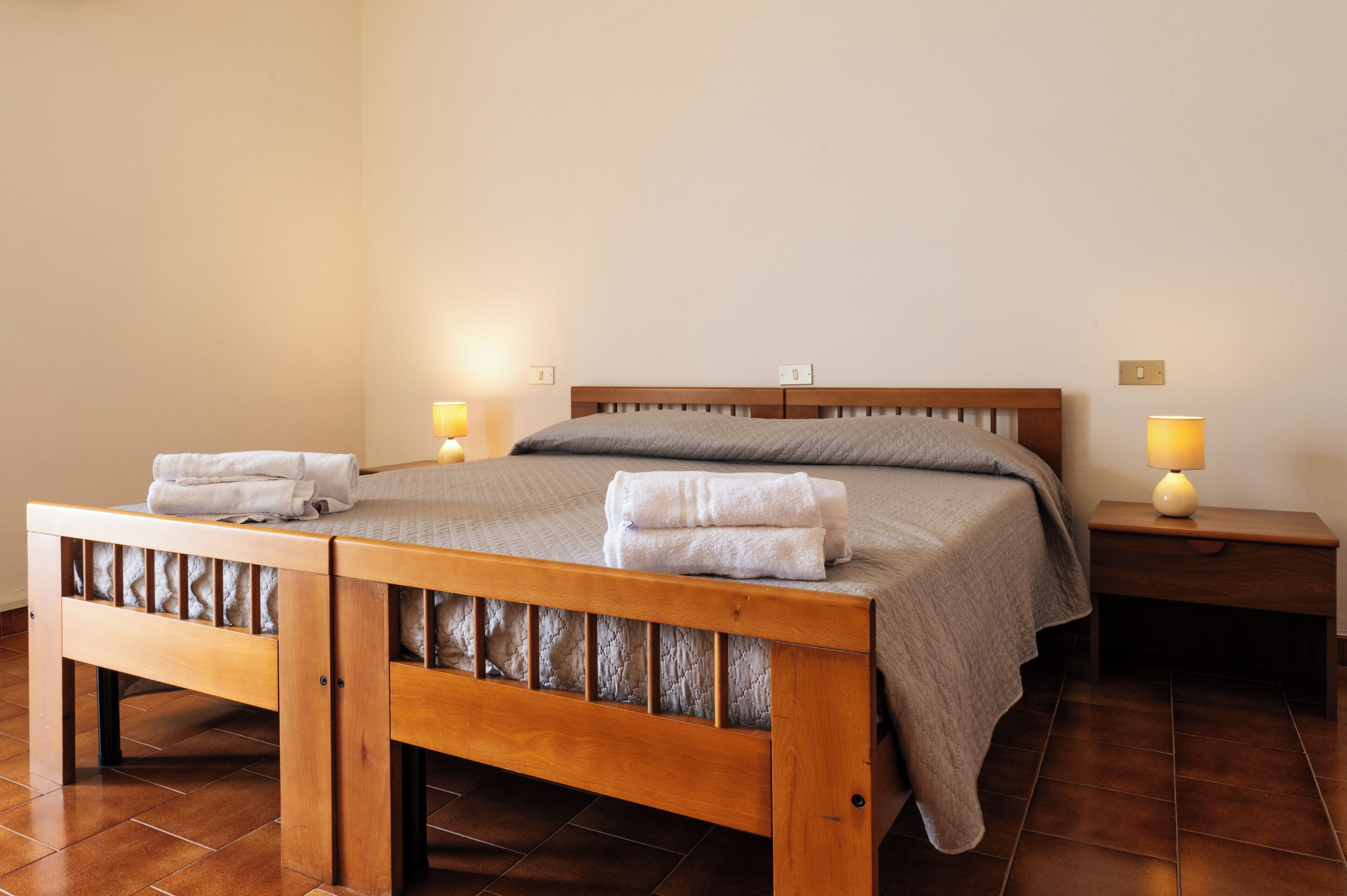 A neatly made bed with pillows and folded towels, a bedside table with a lamp, and a wooden headboard.
