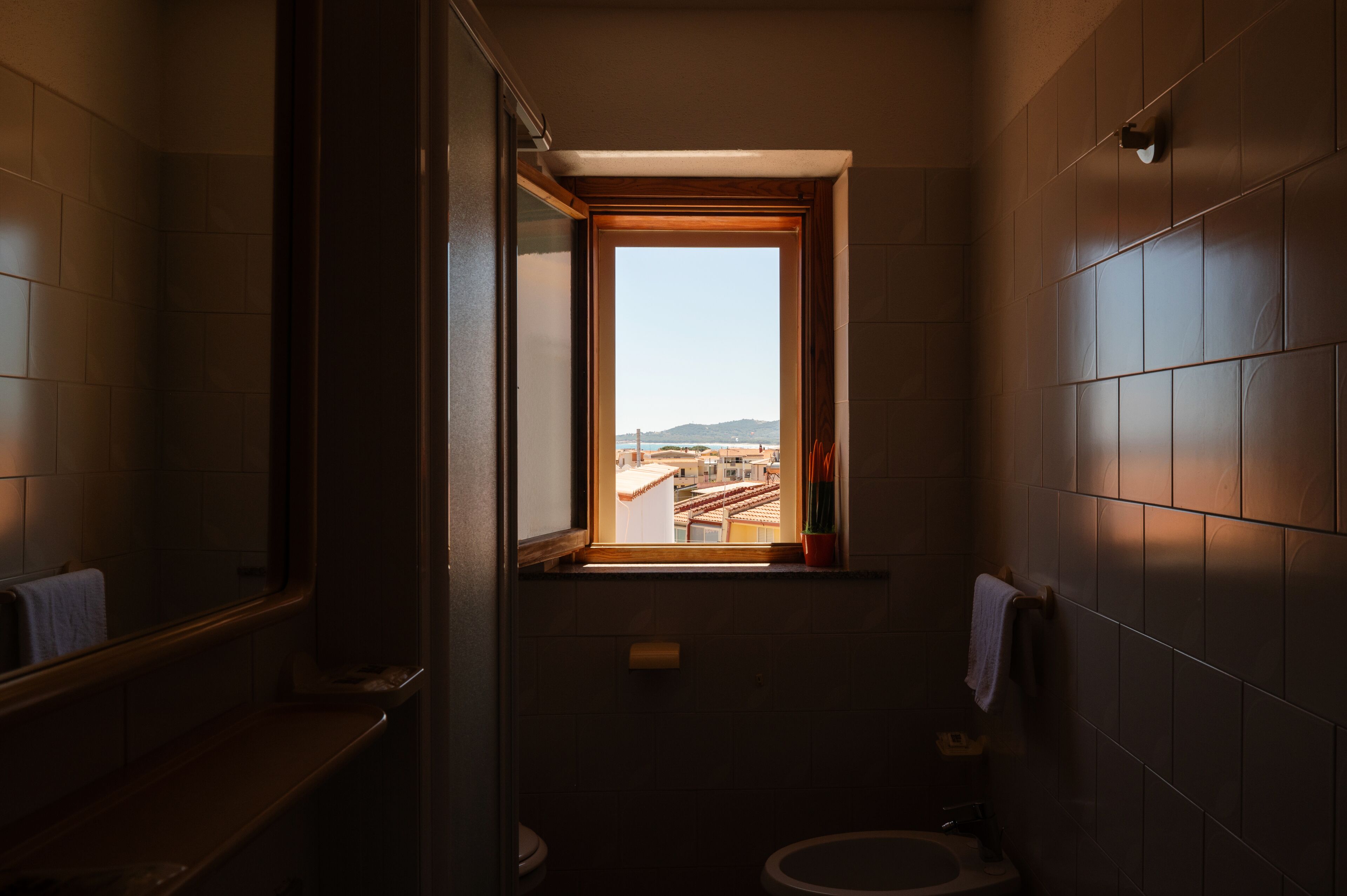 A narrow bathroom with a window providing a view of buildings and a bridge.