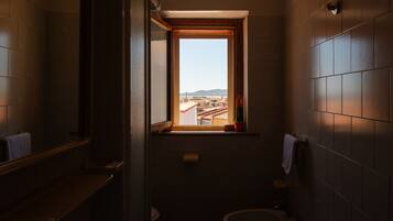 Un baño estrecho con ventana que ofrece vista a edificios y un puente.