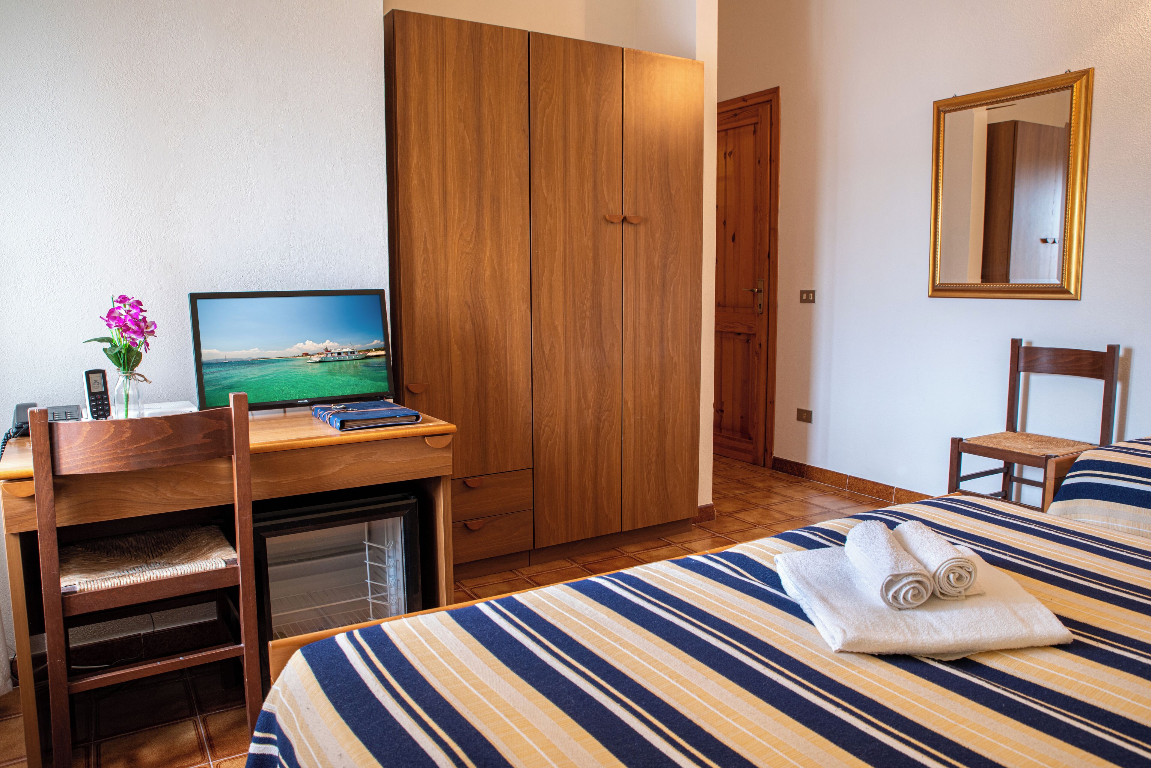 A hotel room with a bed, a desk with a computer, a wardrobe, and a mirror.