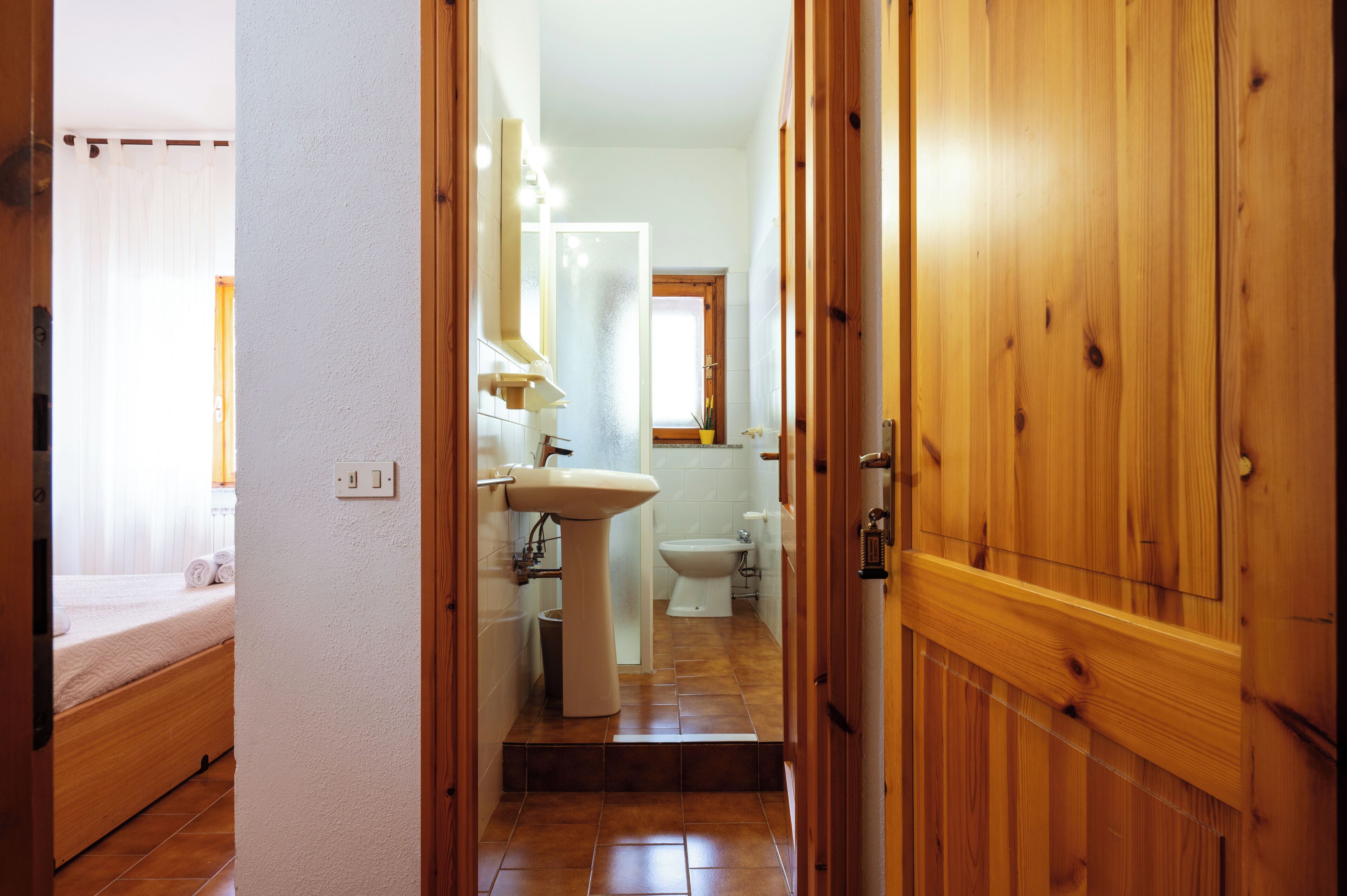 A hallway leading to a bathroom with a sink, toilet, and a bed with rolled towels.