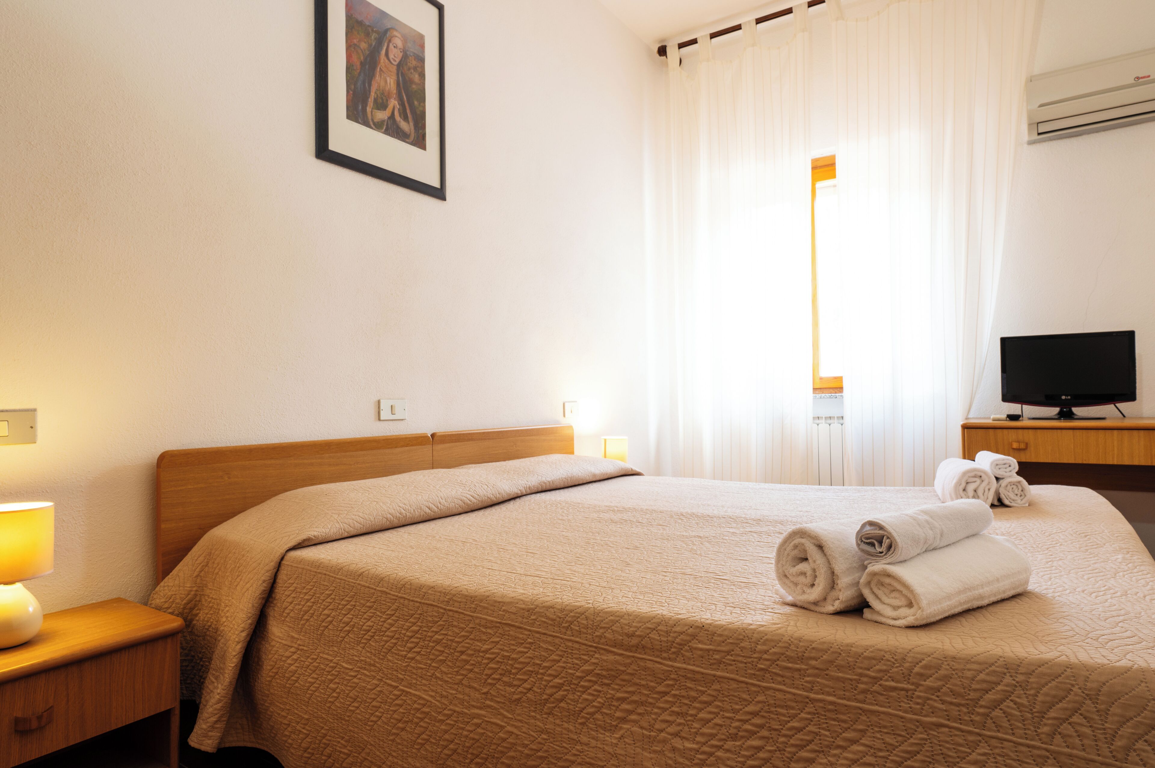 A hotel room with a bed, a bedside lamp, a TV, and a window with curtains.