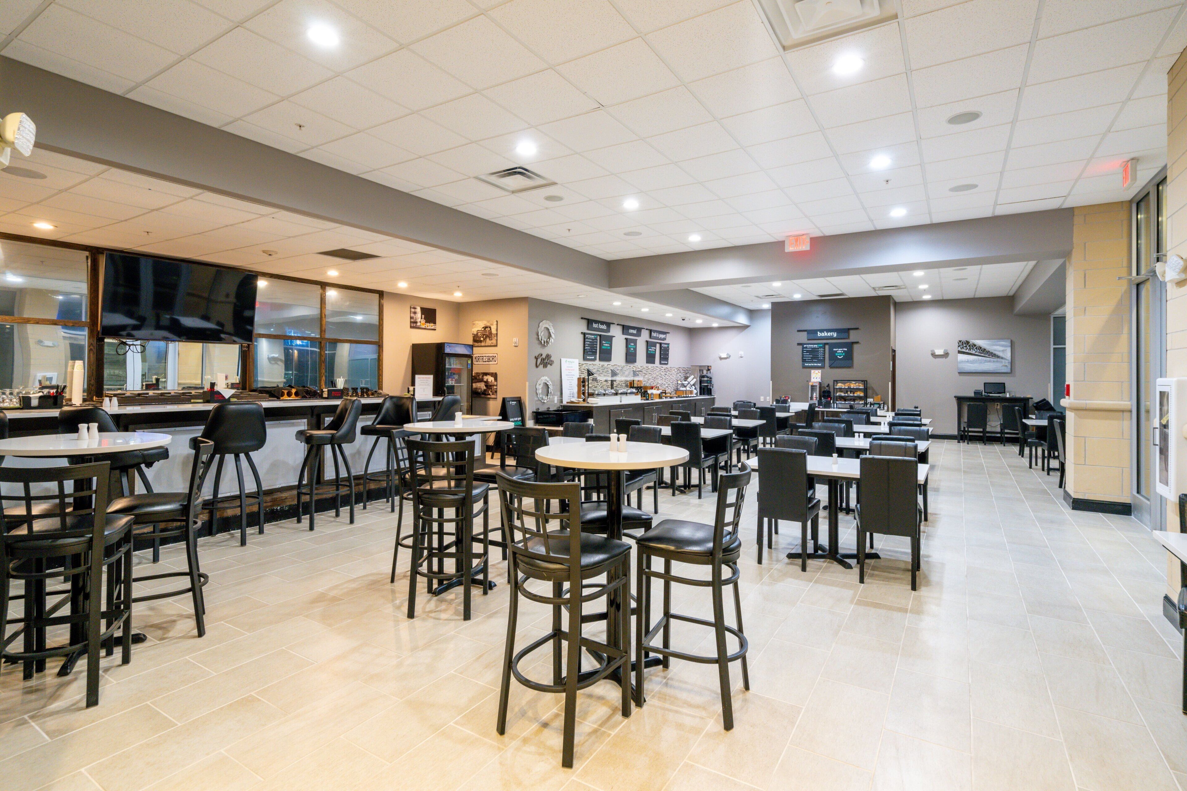 A spacious cafeteria with multiple tables and chairs, a counter with a menu, and a large window providing natural light.