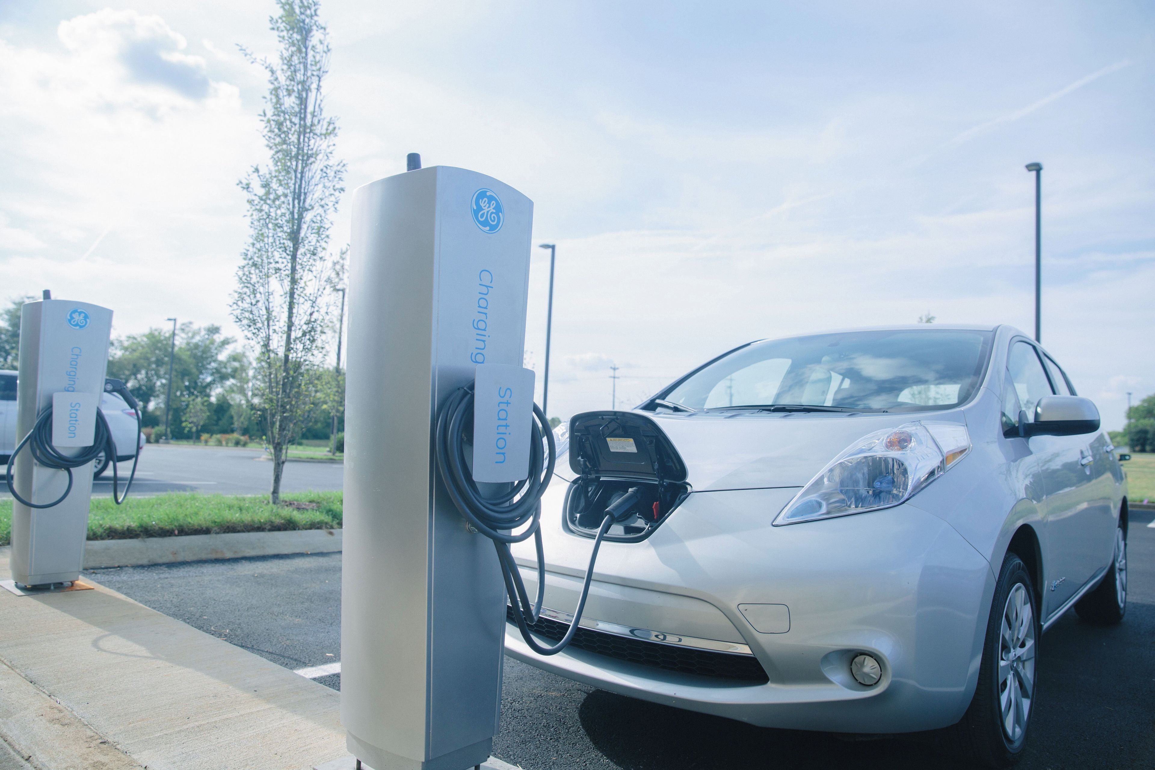 A silver electric vehicle charging at a station with a clear sky.
