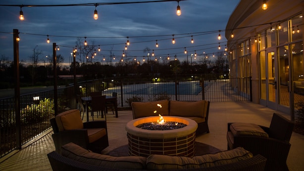 Un área de estar al aire libre con un brasero, rodeada de muebles de mimbre y luces colgantes.
