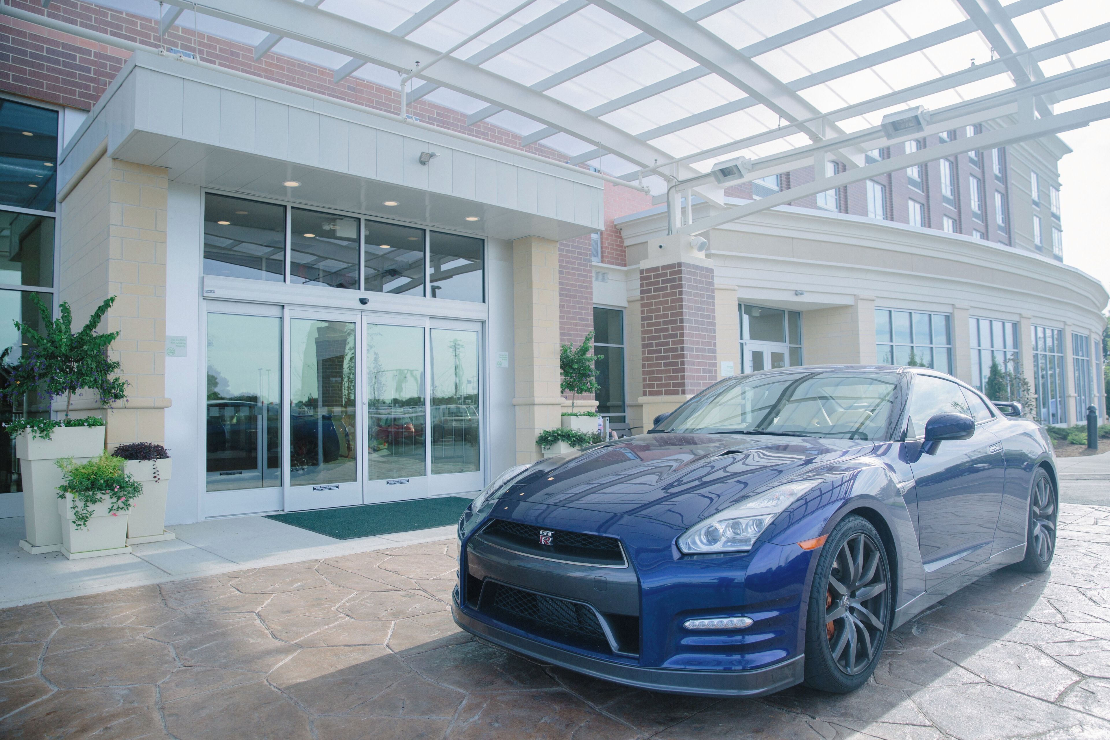 A modern building with a glass entrance and a blue sports car parked in front.
