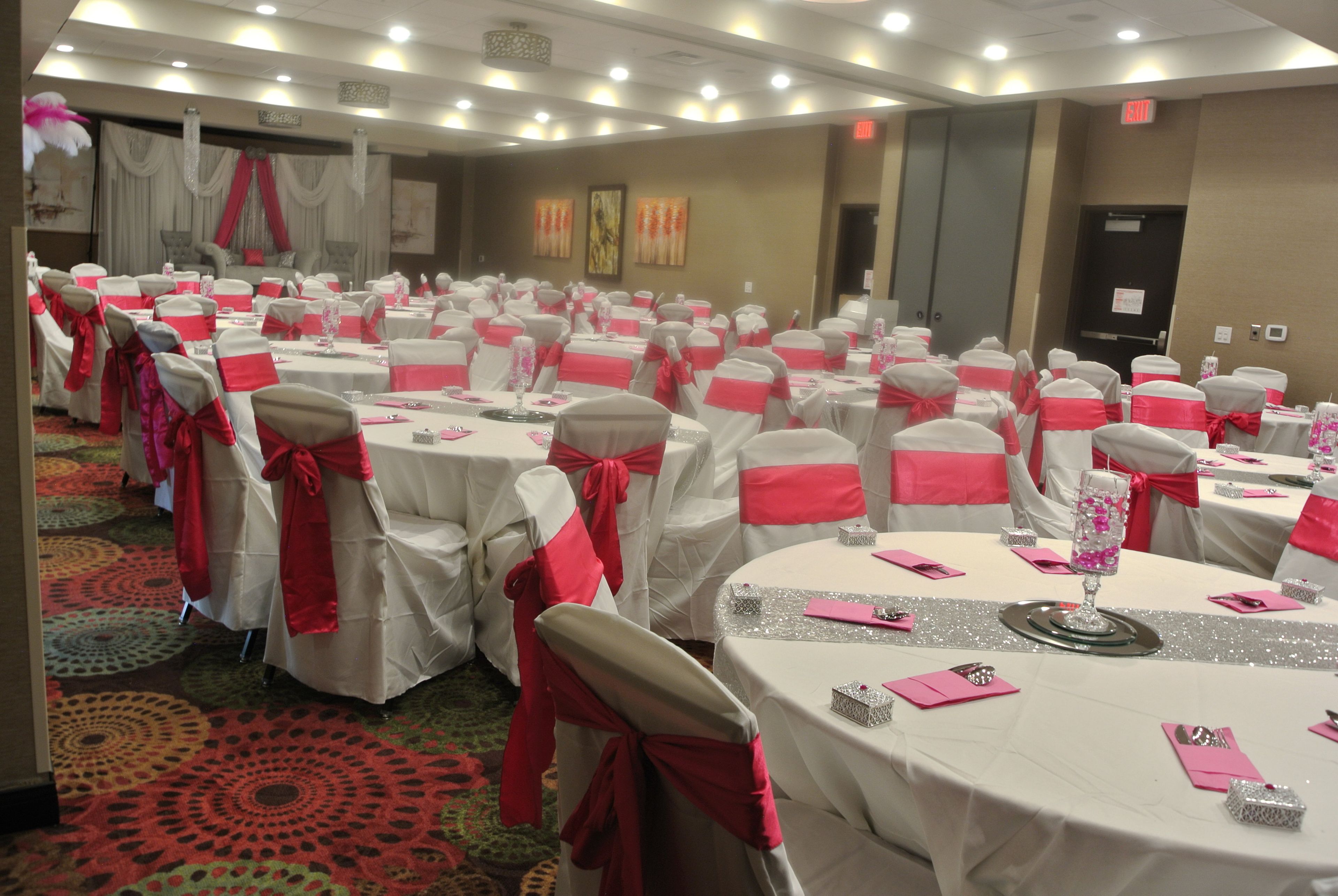 A banquet hall with round tables, each set with white tablecloths and red sashes.