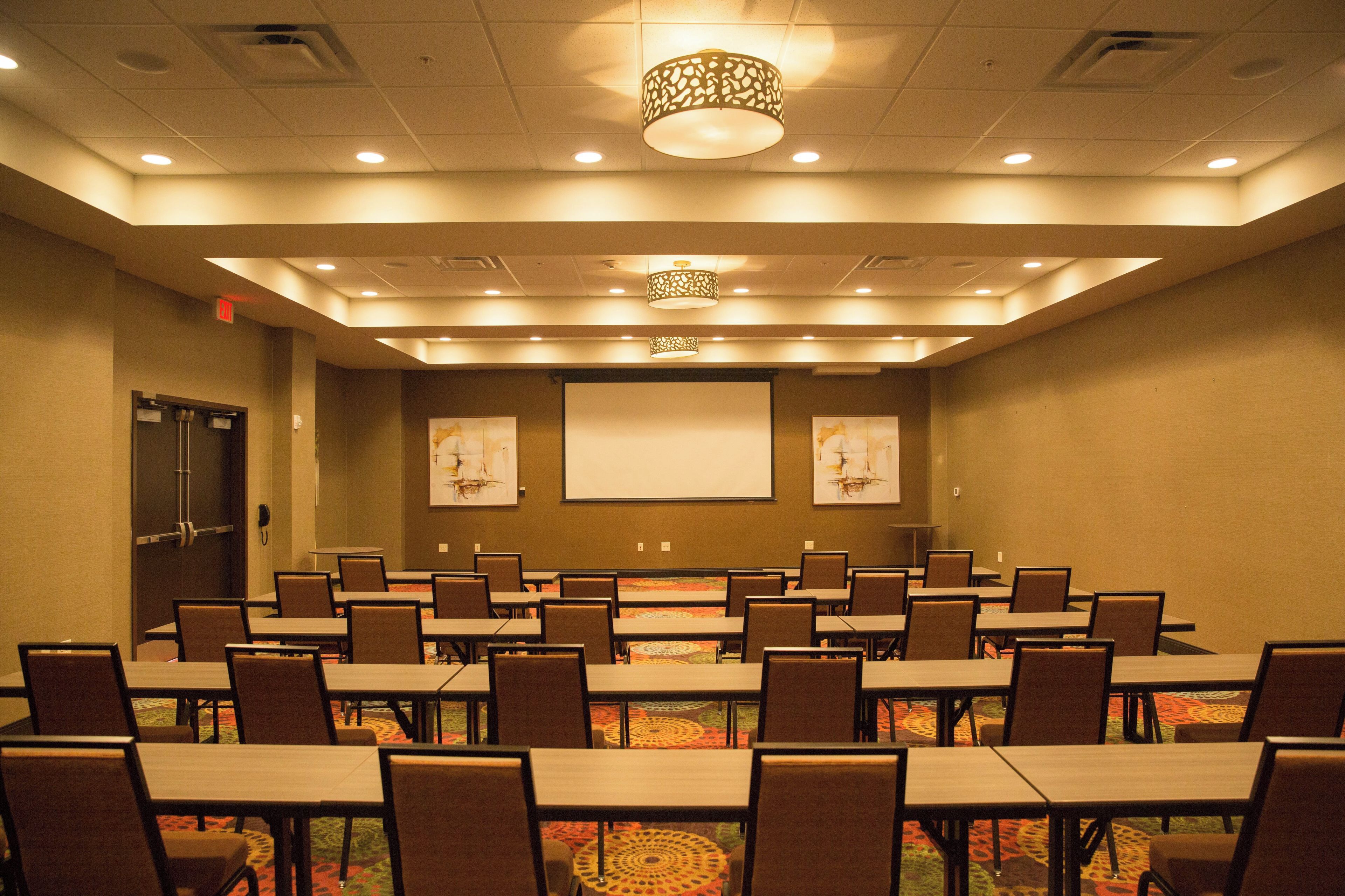 A conference room with multiple tables and chairs, a projector screen, and a patterned carpet.