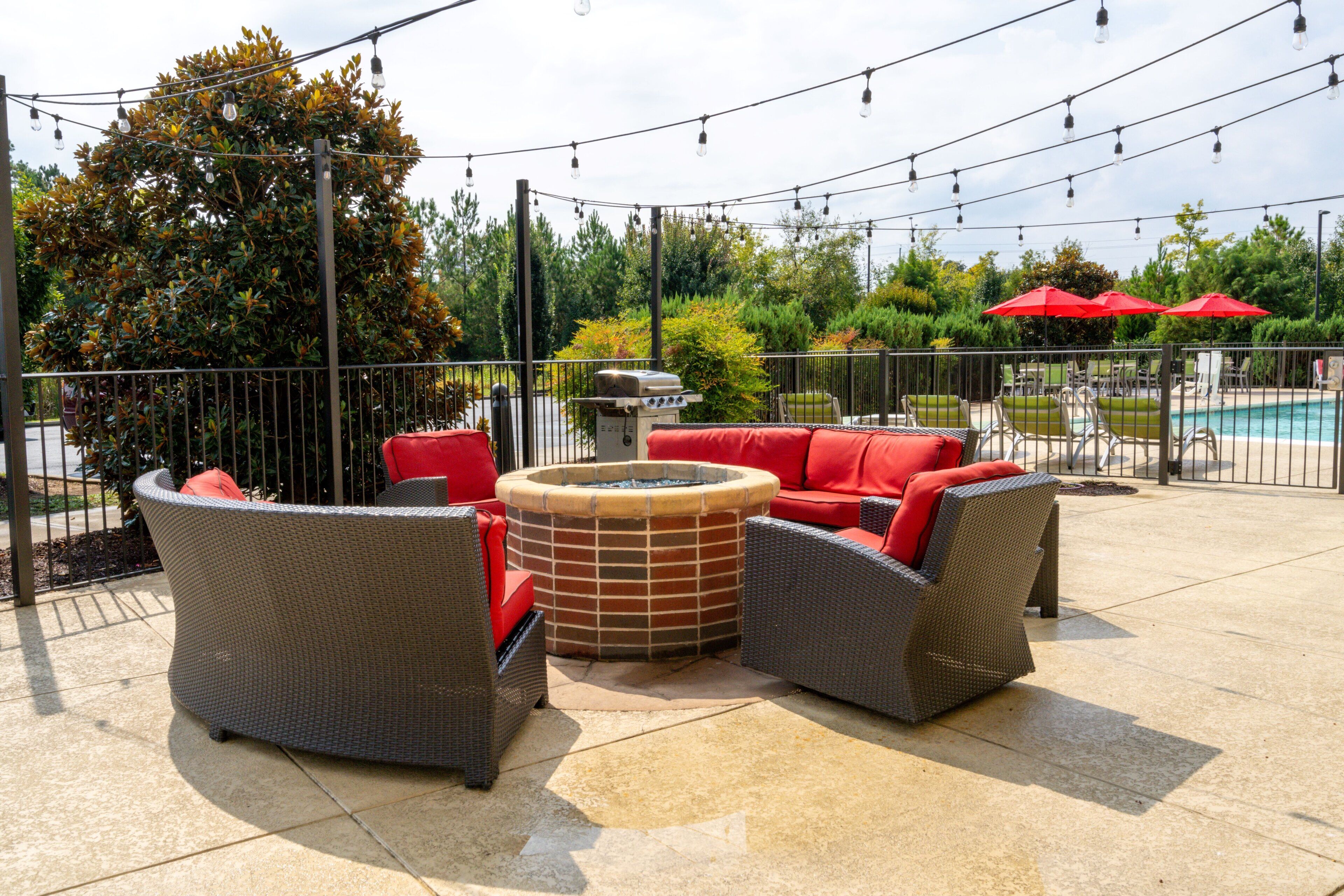 An outdoor seating area with wicker furniture and red cushions, a fire pit, and string lights.