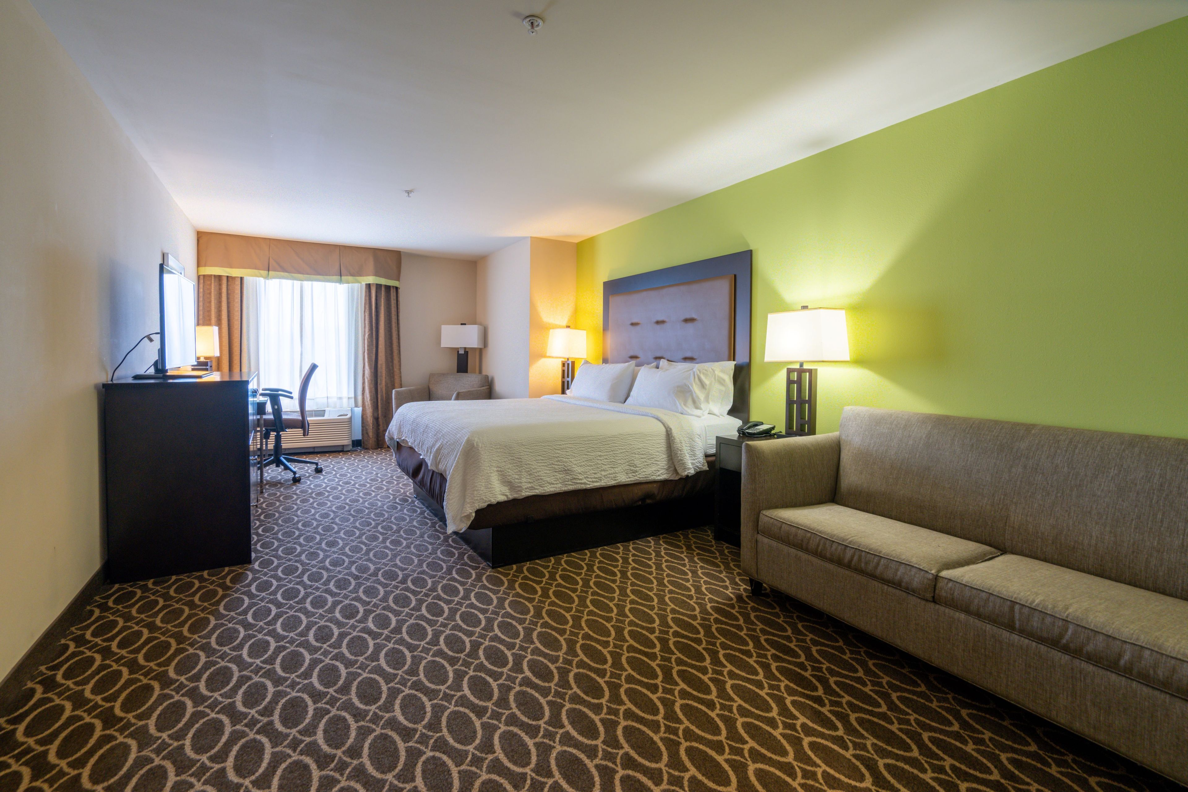 Quarto de hotel com cama, escrivaninha, cadeira, sofá e tapete estampado.