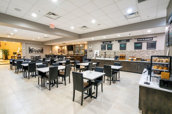 A spacious cafeteria with multiple tables and chairs, a counter with a variety of food options, and a clock on the wall. - Holiday Inn Murfreesboro by IHG (Murfreesboro)