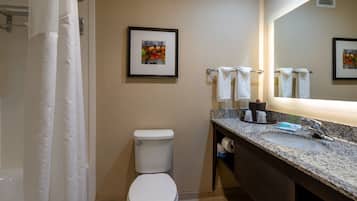 A bathroom with a toilet, sink, and shower curtain. There are towels hanging on a rack and a framed picture on the wall.