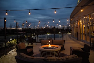 An outdoor seating area with a fire pit, surrounded by chairs and a table, under string lights.