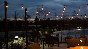 Un patio al aire libre con luces colgantes, un hogar para fuego y vistas a una carretera y un edificio.