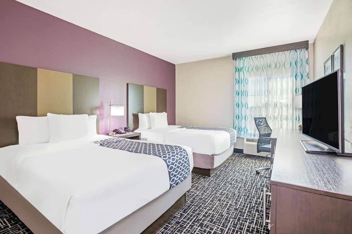 Une chambre d’hôtel avec deux lits, un bureau, une télévision et un sol à motifs.