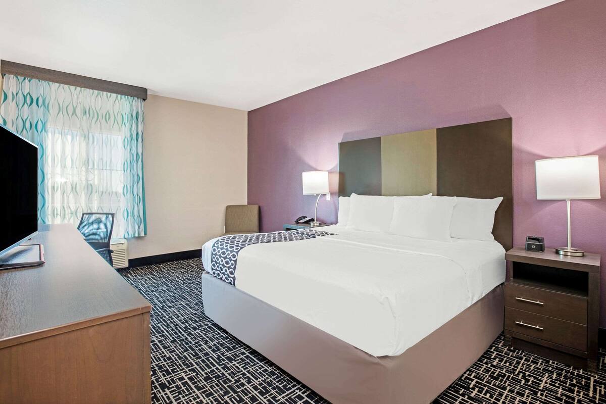 Une chambre d’hôtel avec un grand lit, deux tables de chevet avec des lampes, un bureau et une moquette à motifs.