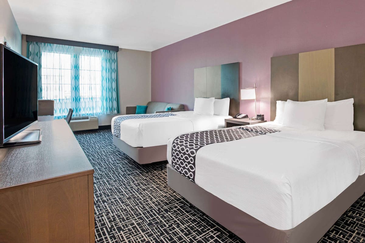 Une chambre d’hôtel avec deux lits, un bureau avec un ordinateur portable, une télévision et une fenêtre avec des rideaux.