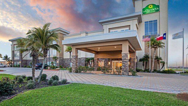 A La Quinta Inn & Suites hotel with a modern design, featuring a covered entrance, palm trees, and a brick pathway leading to the entrance. - La Quinta Inn & Suites by Wyndham Corpus Christi - Portland (Portland)