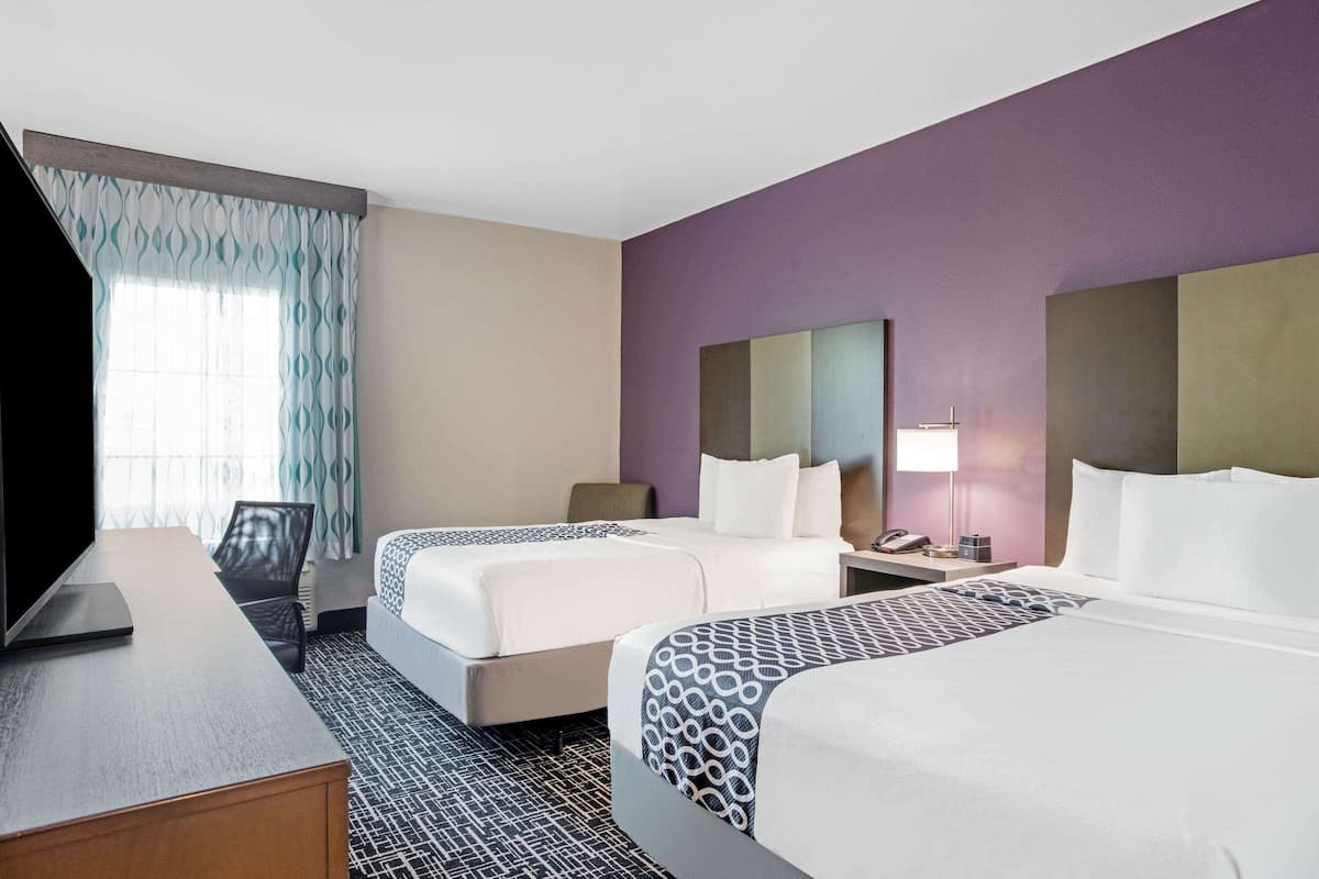 Une chambre d’hôtel avec deux lits, un bureau, une chaise, une télévision et une fenêtre avec des rideaux.