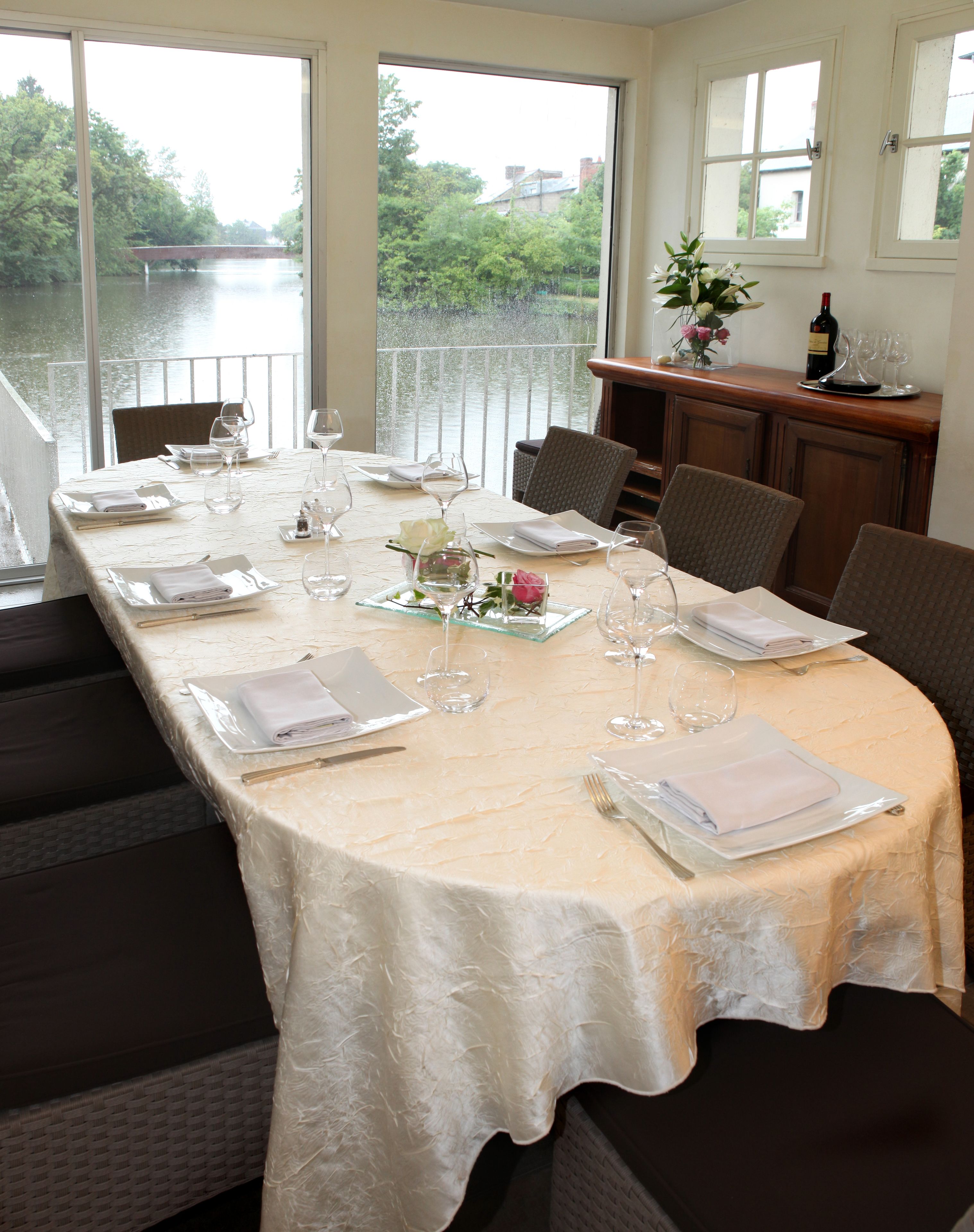 Une table à manger dressée pour six personnes, avec vue sur une rivière et un pont.