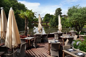 An outdoor dining area with tables and chairs, surrounded by umbrellas and greenery. - Le Germinal (Cesson-Sevigne)