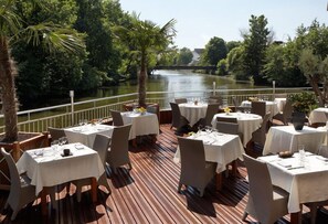 An outdoor dining area with tables and chairs, overlooking a river.