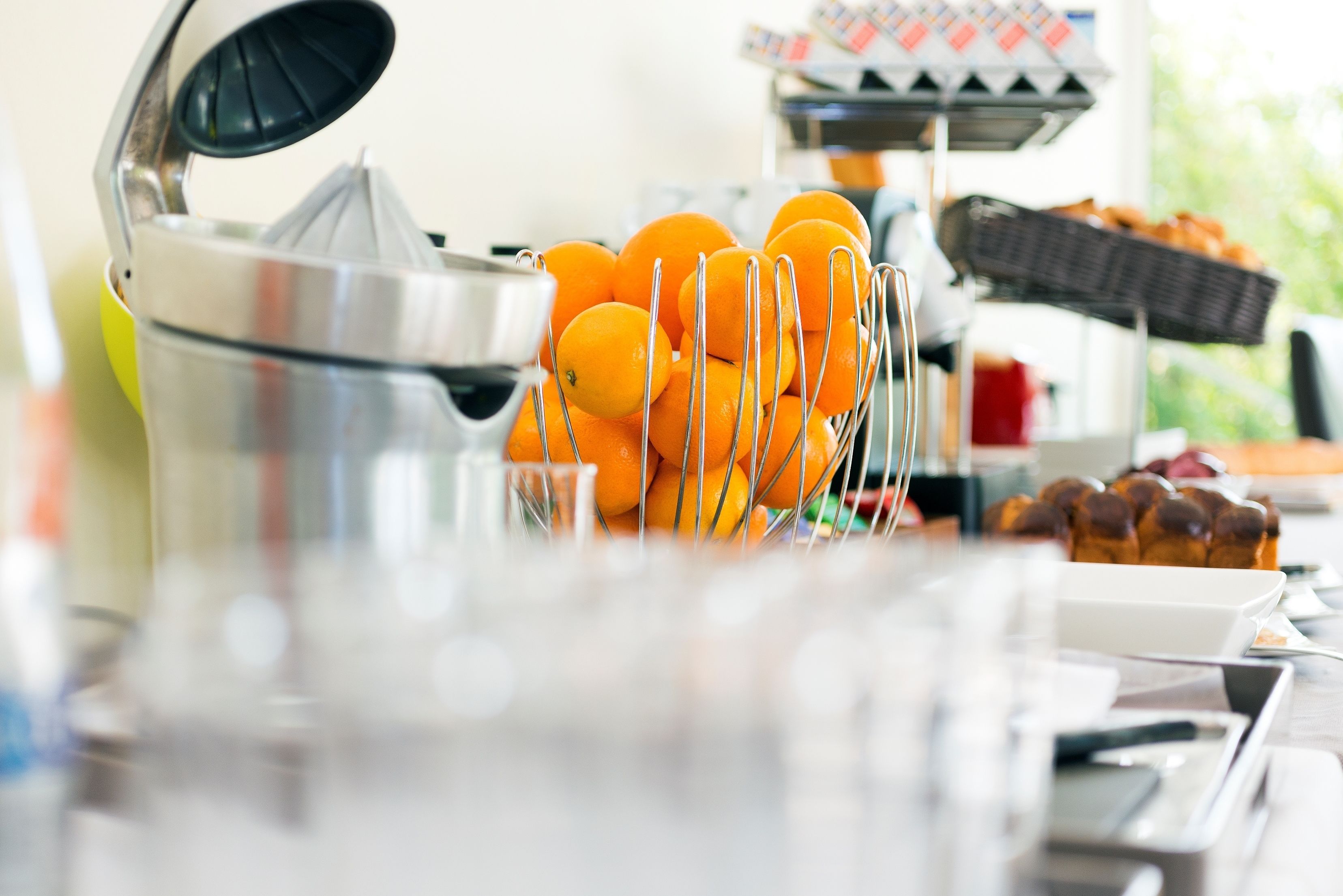 A juicer with oranges, a tray of pastries, and a coffee maker on a table.