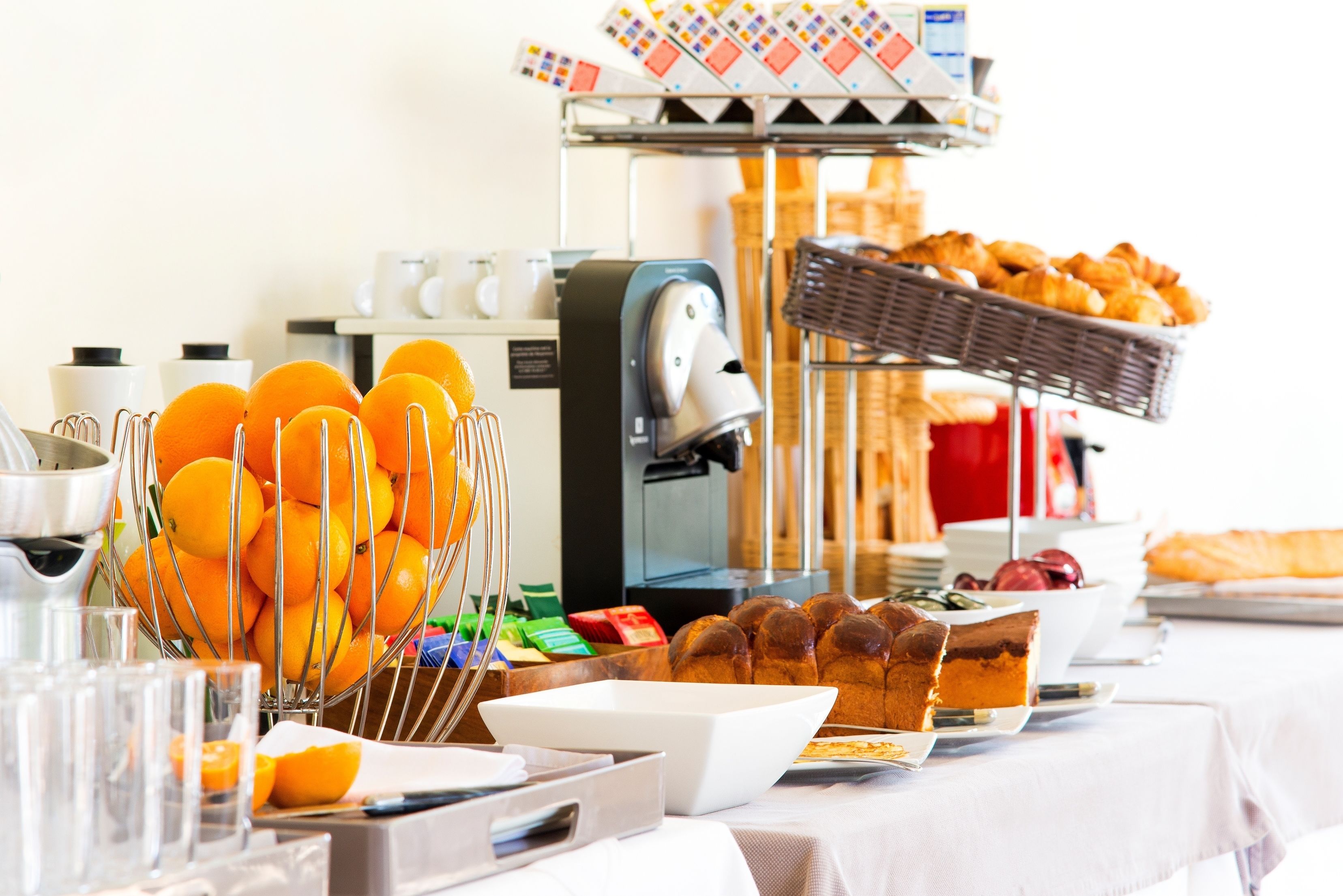 A buffet table with various food items, a coffee machine, and a basket of oranges.