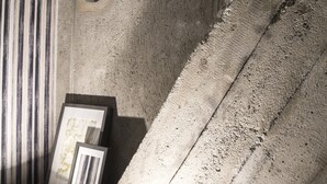 A modern interior with a textured concrete wall, a striped bench, and framed pictures. - Serendipity Rooms (Milan)